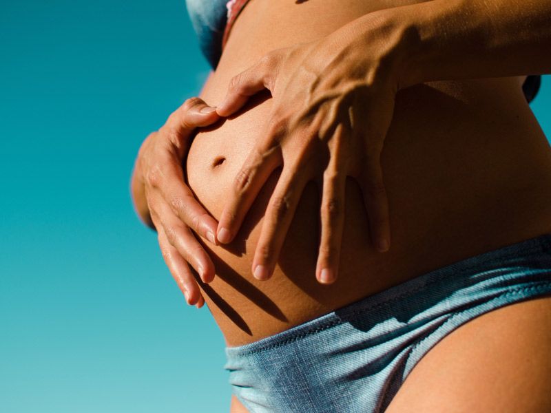 a pregnant woman in a blue bikini holding her stomach against a blue background