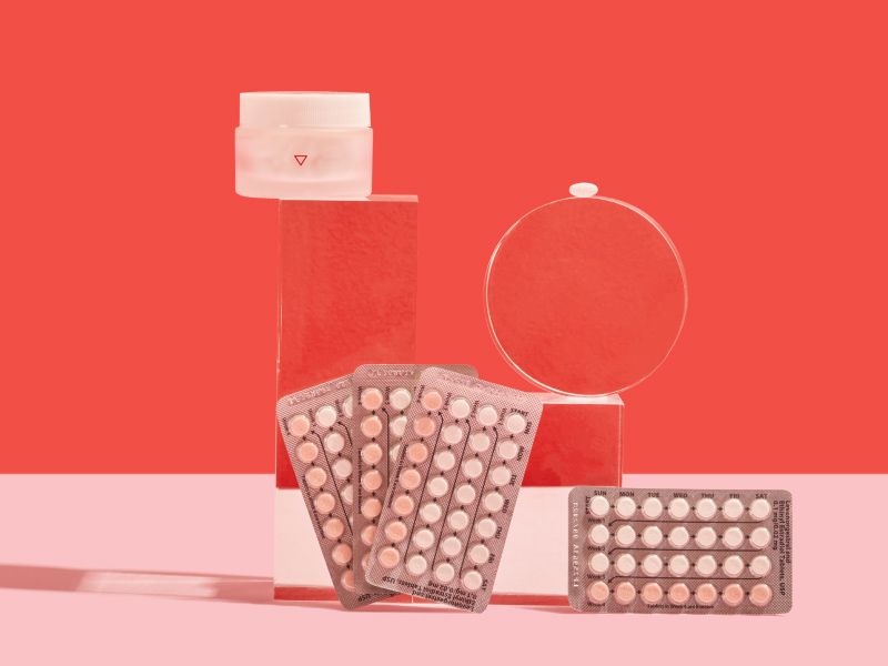 Birth control packets and a Wisp medication jar on a pink and red background
