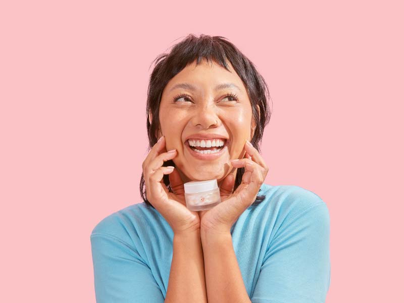 A female wearing a blue shirt holding a Wisp small glass pill jar with a smile on her face