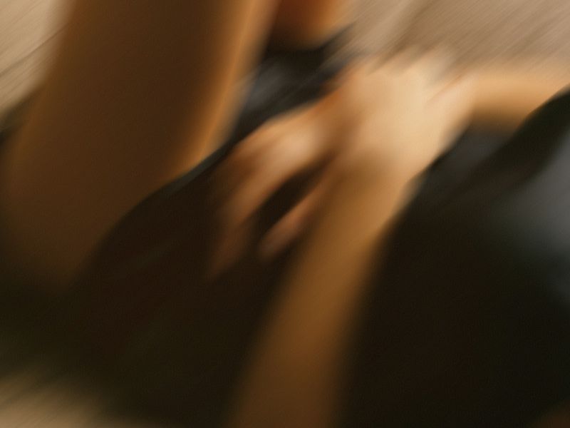 Close-up, motion-blurred image of a person sitting and holding their stomach, suggesting abdominal discomfort.
