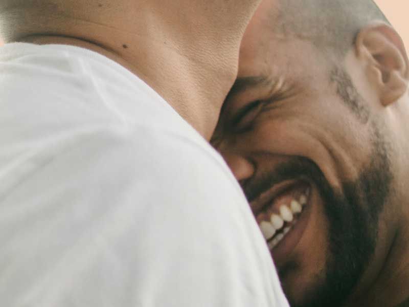 Close-up of a smiling person partially hidden behind someone’s shoulder