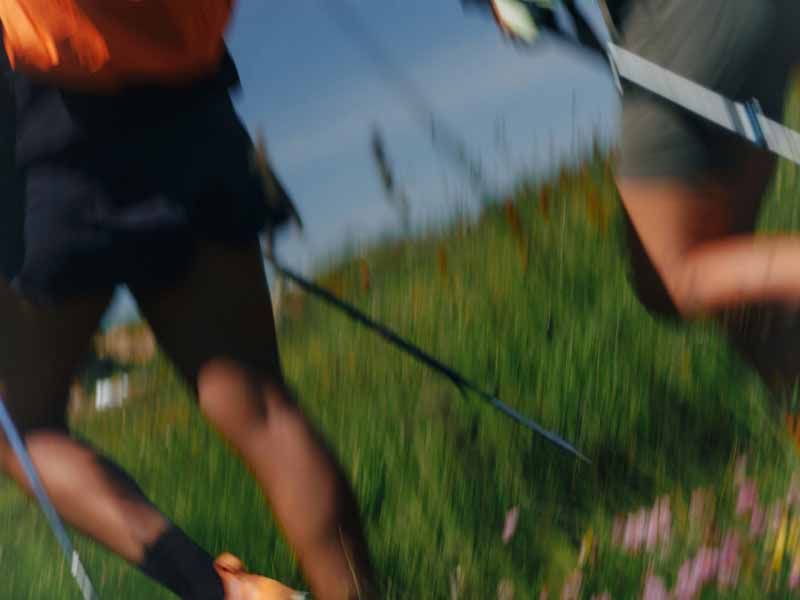 Blurred shot of legs moving through a green field with a leash or strap in hand.