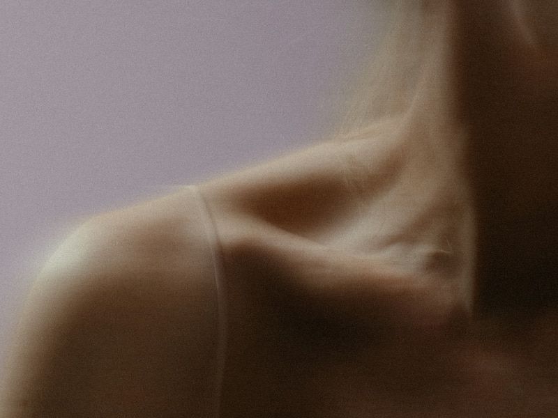 A softly blurred close-up of a person's shoulder and neck area against a muted background.