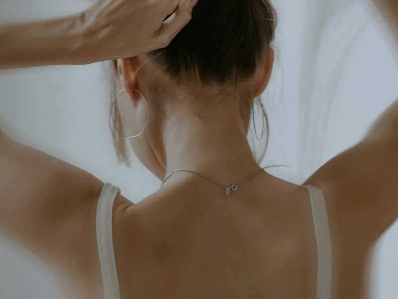 Close up of the back of someone raising their arms while wearing a white top