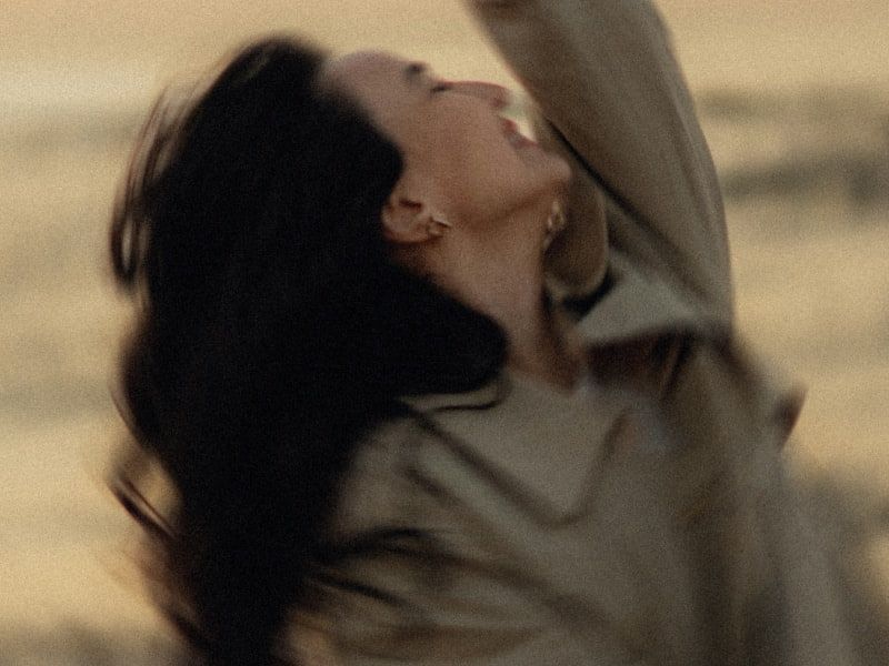 A woman with dark hair tilting her head back, captured in a cinematic, warm-toned close-up.