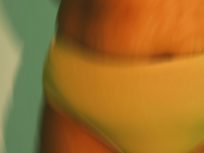 A close-up of a person's midsection wearing yellow bikini bottoms against a teal background.
