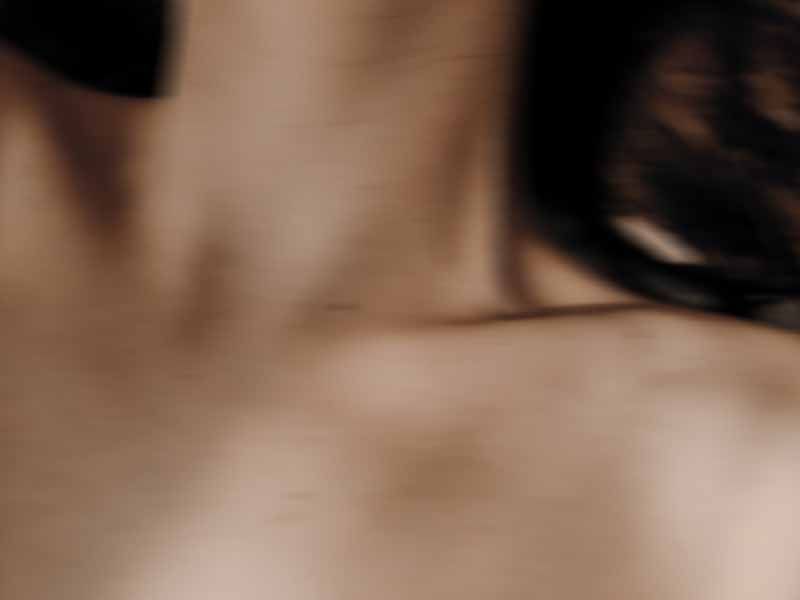 Blurred close-up of a neck and collarbone with dark hair in motion and warm, moody lighting.