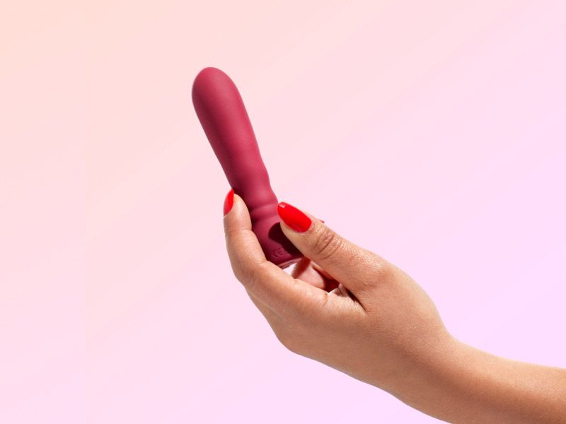 Hand holding a vibrator on a orange and lilac gradient background