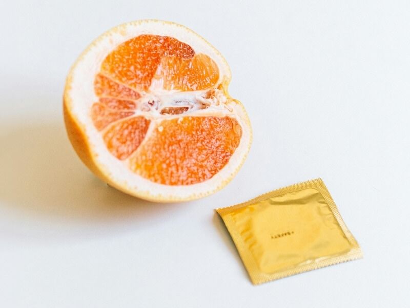 a white background with half an orange facing outwards next to a gold foil square packet