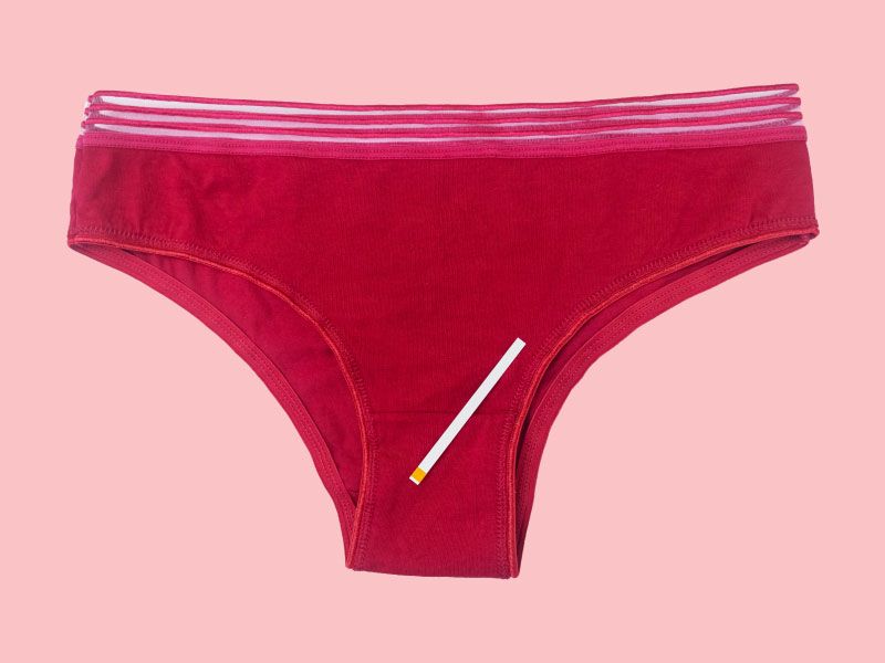 A pair of dark red women's underwear with a test strip laying on top on a pink surface