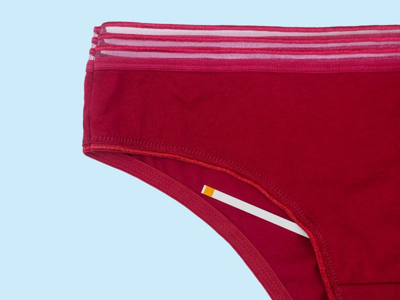 A pair of dark red women's underwear with a test strip laying on top on a blue surface