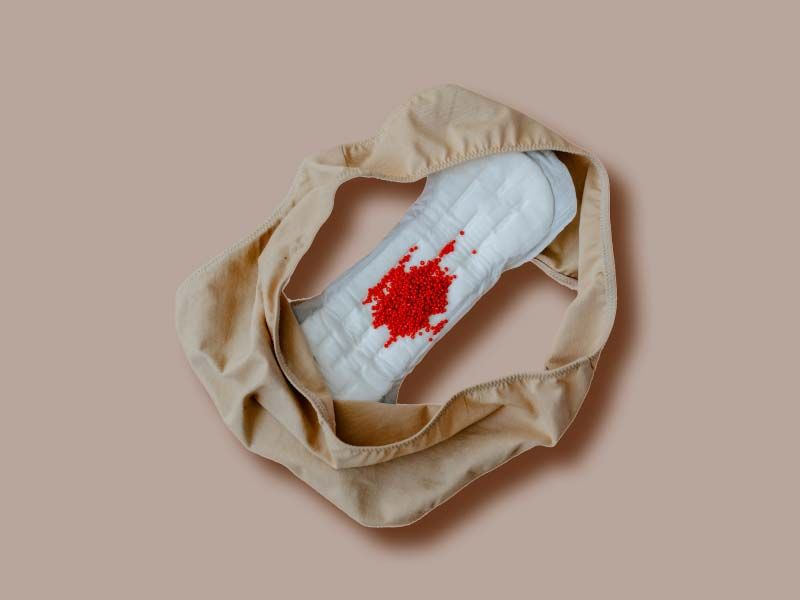 A pair of underwear and a menstrual pad with red glitter on it on a beige surface