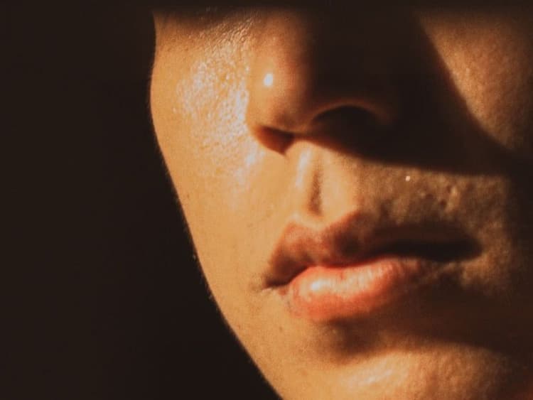 Close-up of a person’s lower face, lit by warm light against a dark background.