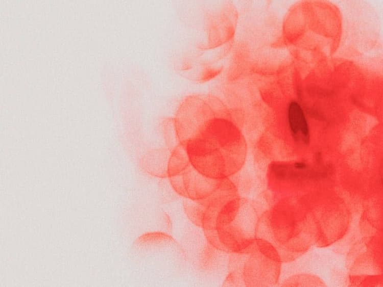 Abstract grainy texture of overlapping translucent red circles clustered on the right, fading into a pale off-white background.