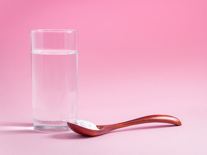 Glass of water and wooden spoon full of mixing powder on pink gradient background