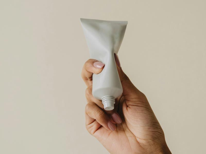 A person's hand holding a white tube in front of a beige background