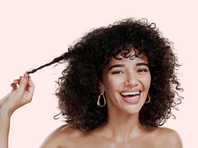 A smiling woman with luscious thick curly hair in front of a peach-colored background