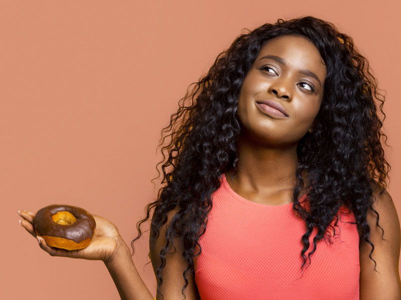A pretty woman wearing a red shirt looks contemplative while holding a donut
