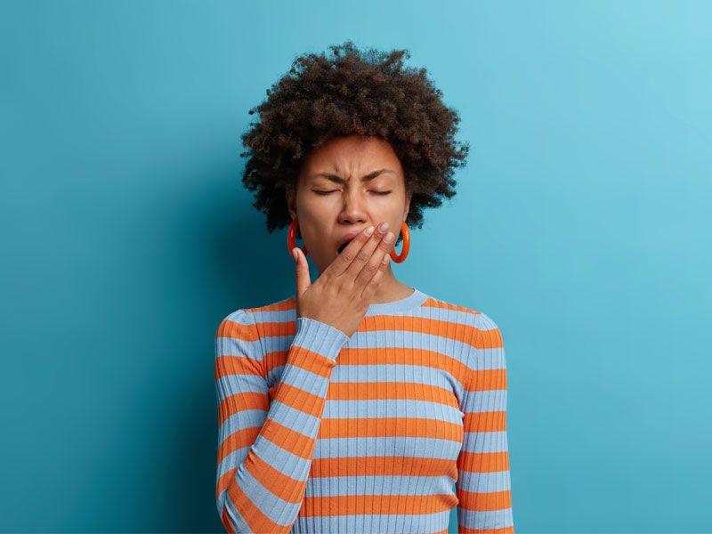Woman in striped sweater yawning with teal background