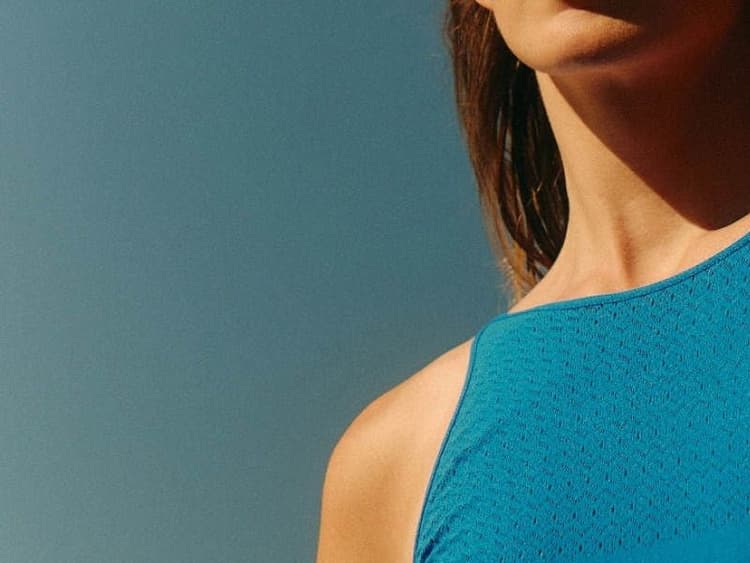 Close-up profile view of a woman's neck, showing the throat area, against a teal background.
