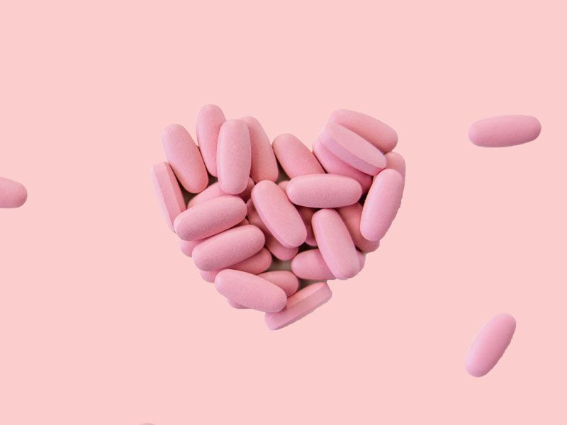 Pink oval-shaped pills grouped together in the shape of a heart on a pink surface