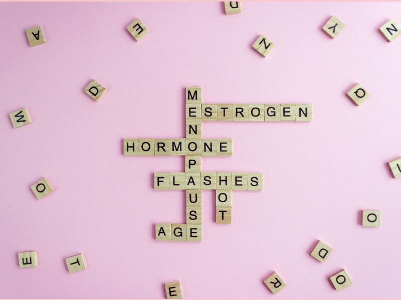 Scrabble tiles spelling out. menopause symptoms with various scattered tiles around it on a purple surface