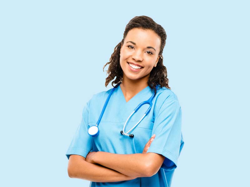 A female medical professional who is smiling and wearing blue scrubs and a stethoscope