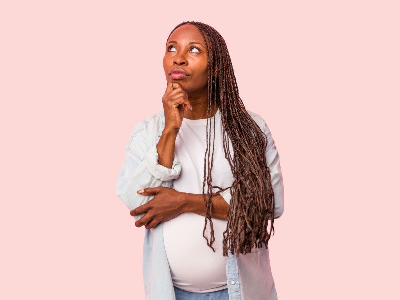 A pregnant woman wearing a white shirt is looking contemplative in front of a pink background