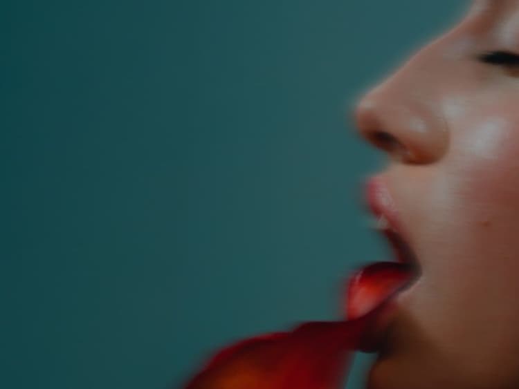 Side profile of a person with tongue out, a red petal resting on it, against a teal background.