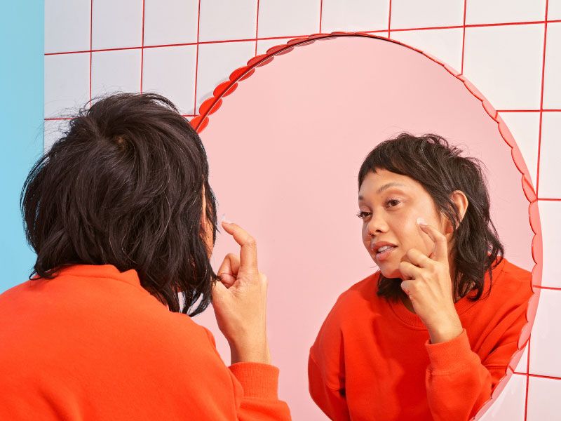 A woman looking into a mirror with a red frame on a white and red tile wall