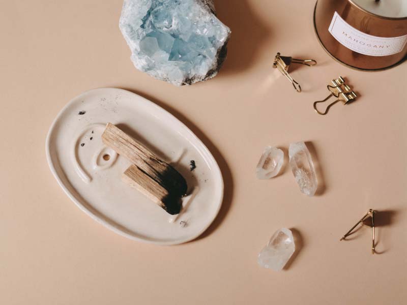 A tray with burnt palo, gemstones and a candle on a tan surface