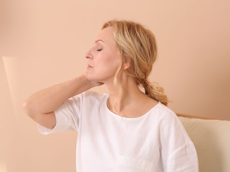 A woman with blonde hair and wearing a white shirt has her hand on the back of her neck and looks stressed