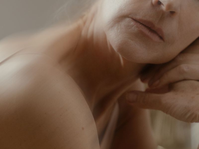 Close-up, artistic image of a person's lower face, neck, and bare shoulder, softly lit with warm tones, evoking themes related to hormone replacement therapy.