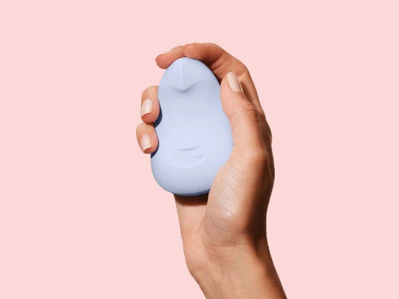 A woman's hand holding Dame Pom Flexible Vibrator in front of a pink background