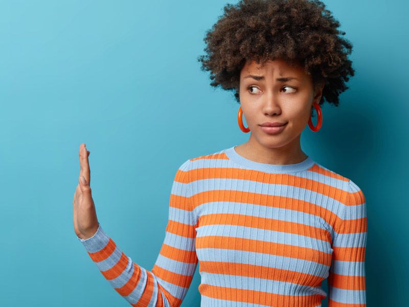 a woman in a striped sweater raises her hand and gives side eye on a blue background