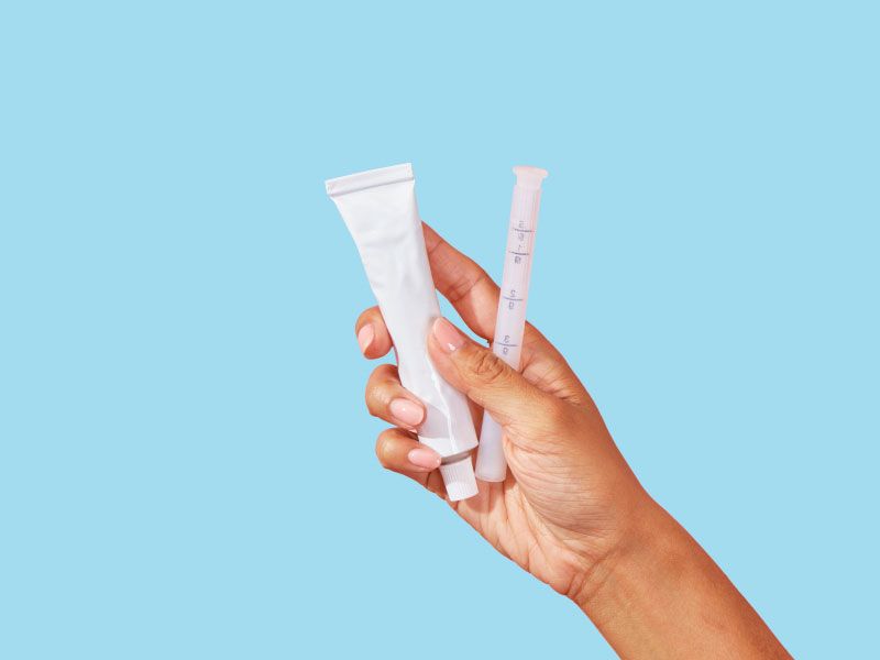 A person's hand is holding a tube of hemorrhoid cream in front of a light blue background