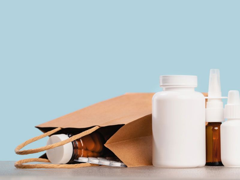 Various medication bottles and a paper bag with medications spilling out on a gray surface with a green background