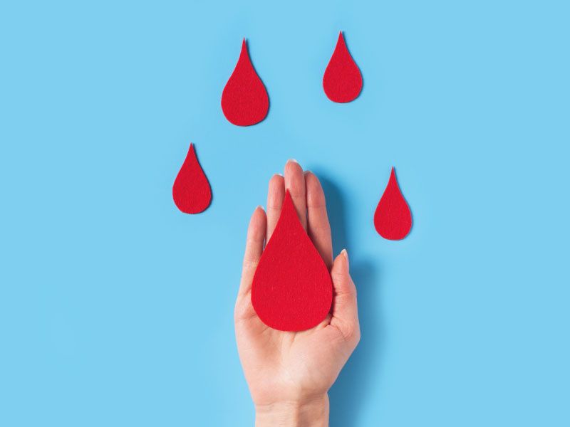 A hand with blood drop cutouts on a light blue surface