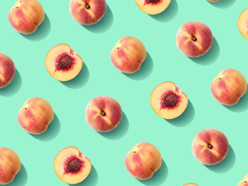 Whole and halved peaches laid out in rows on a bright green surface