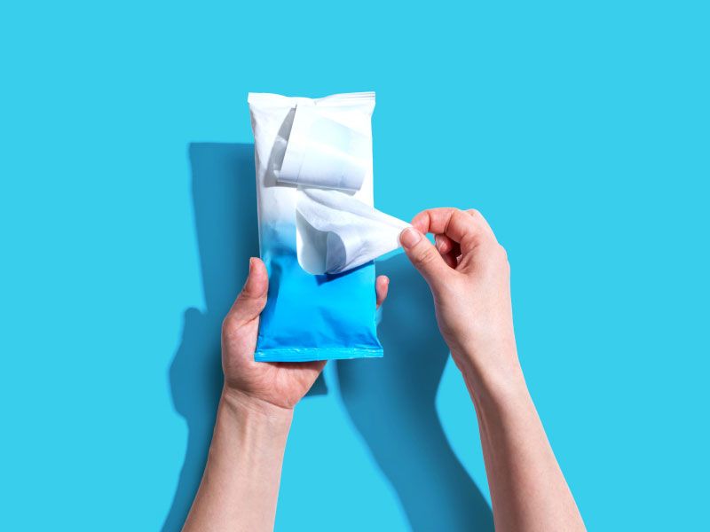 A person's hands holding sanitary wipes on a bright blue surface
