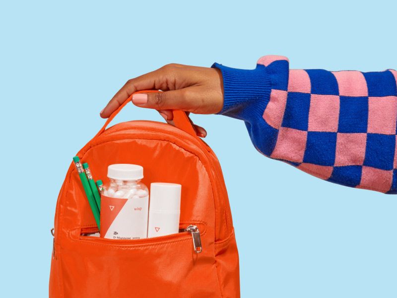 a woman's hand holding a red backpack with Wisp meds inside on a blue background