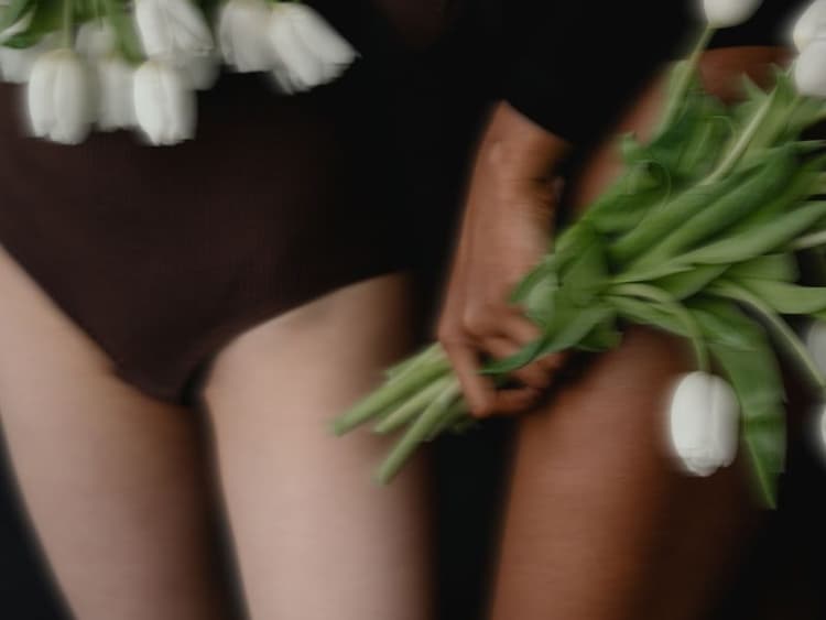 Close-up of a bare leg and hip, with a hand holding white tulips against the thigh; soft, blurred, artistic style.