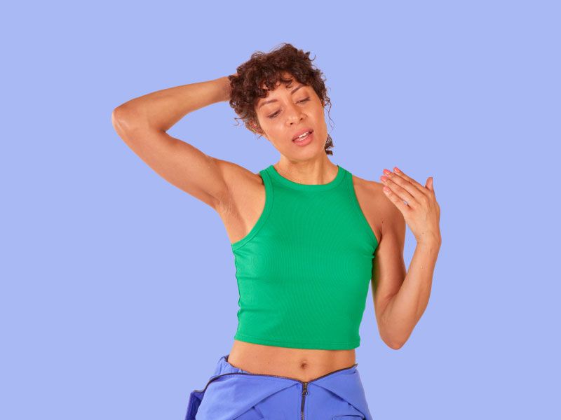 A woman wearing a green tank top and blue pants is holding her hair up and fanning her face