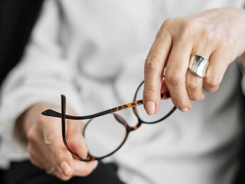 A woman wearing a white button up shirt is holding her glasses with a strained look on her face