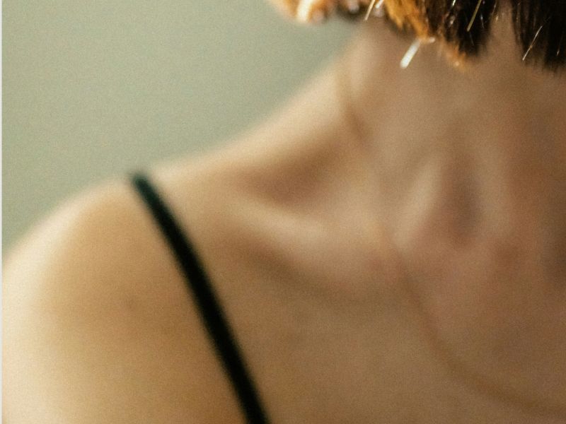 Close-up of a person’s shoulder and neck in a black spaghetti-strap top against blurred background