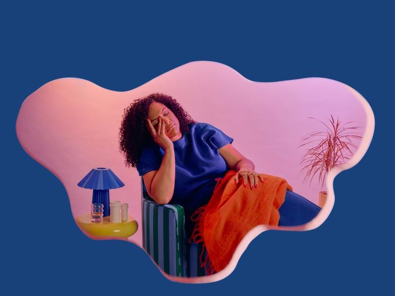A woman sitting on a blue sofa with her hand on her face in discomfort