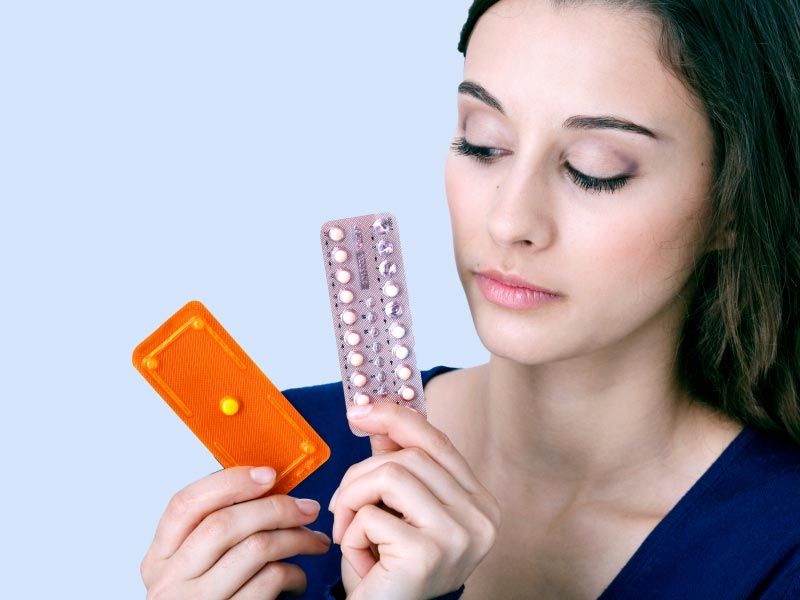 Woman holding an Emergency Packet and a Birth Control packet or a gray blue background