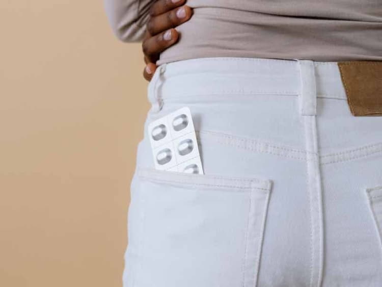 A woman wearing white jeans with a pill packet in her back pocket