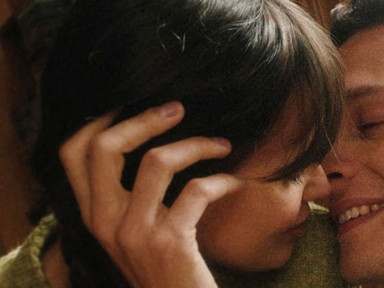 image of woman affectionately embracing a smiling man, nuzzling his cheek, in a warm, softly lit setting