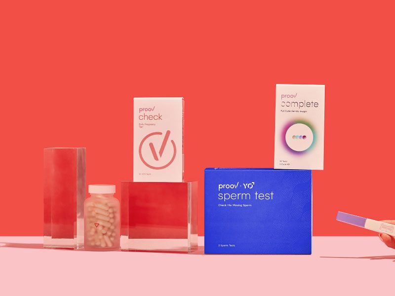 Proov Complete and Hers & His Testing kits next to Wisp Prenatal Vitamins and Pregnancy test on a pink surface with a red background